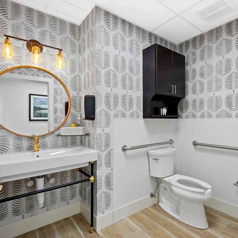 The patient restroom, with patterned wallpaper and a round brass mirror.